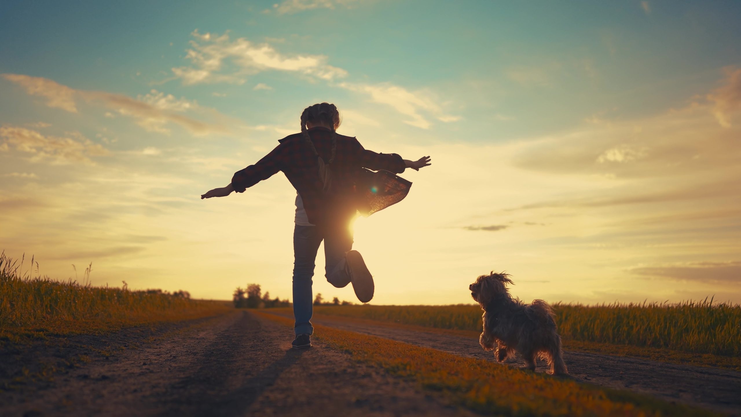 Child and dog running towards sunset