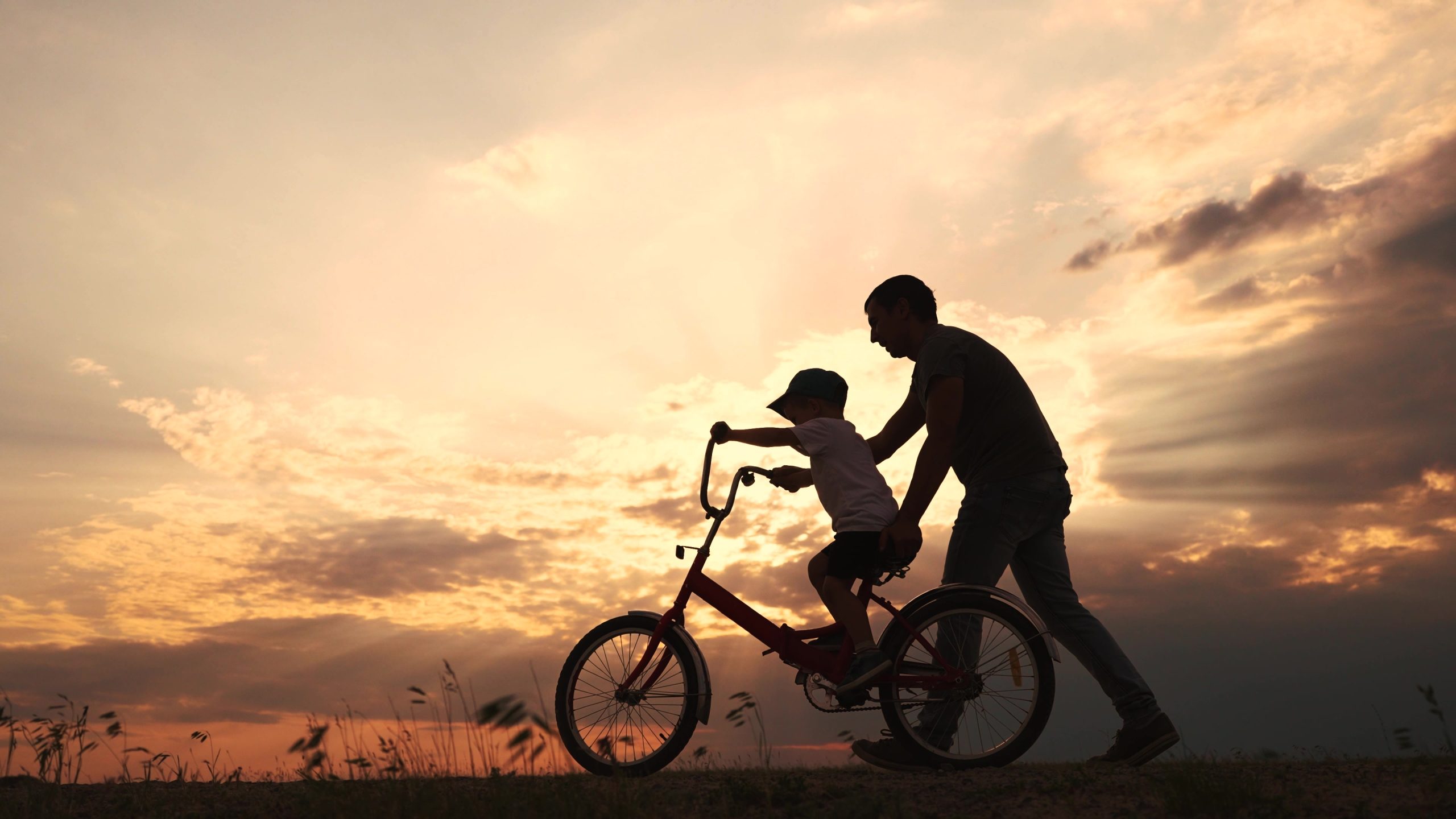 Father teaches his son to ride a bike, at sunset