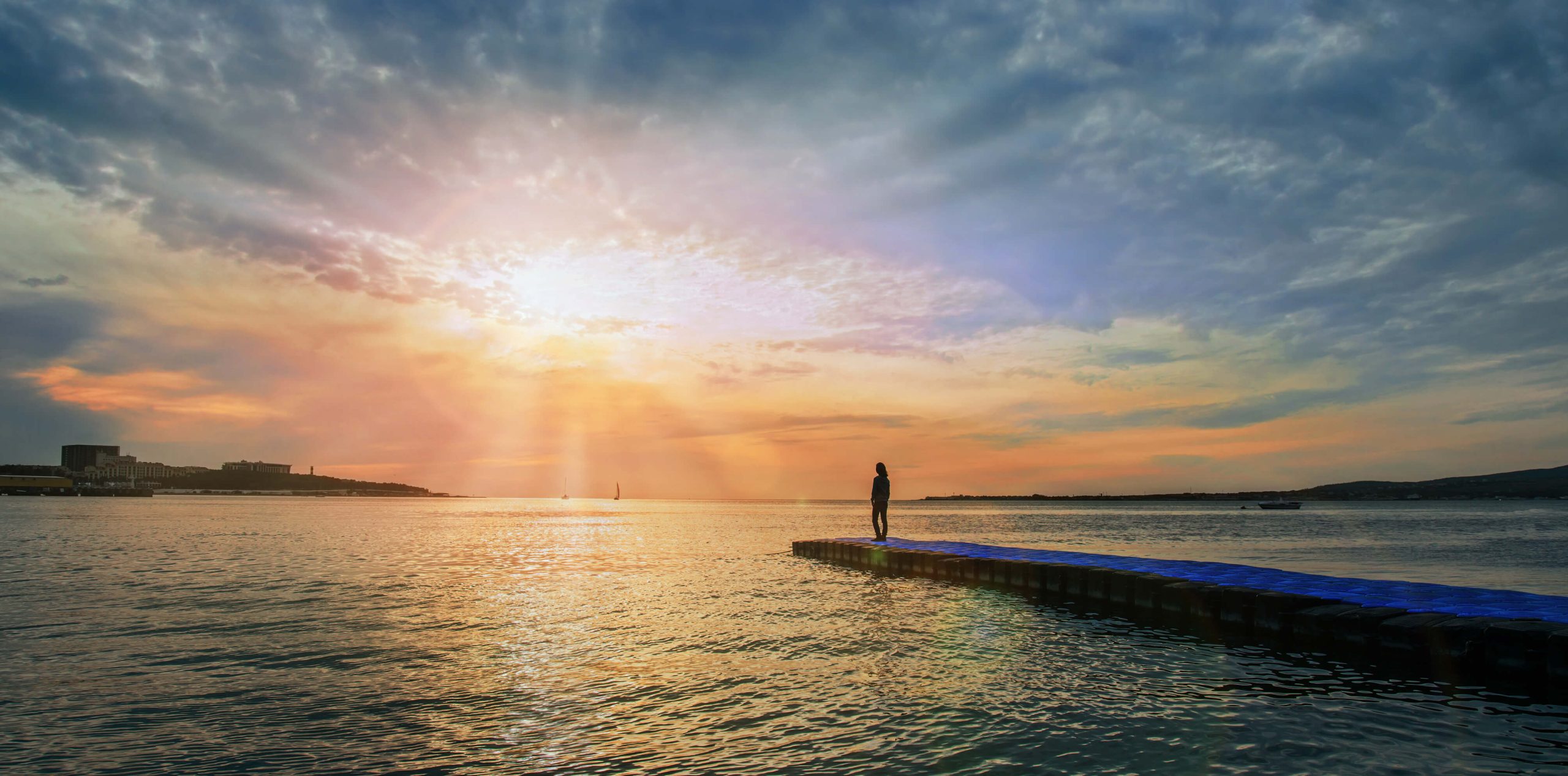 Woman stood on pier on-top of the sea, looking at the sunset